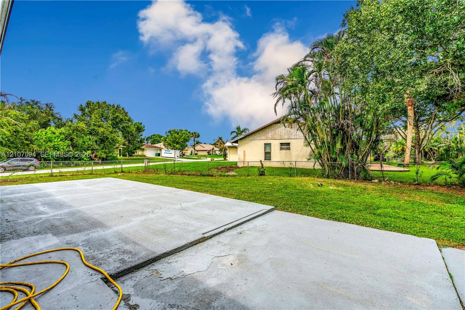 1131 SW London Lane, Port St Lucie, FL 34953 Spacious concrete patio overlooking a backyard featuring a grass lawn, mature palm trees, and metal perimeter fencing