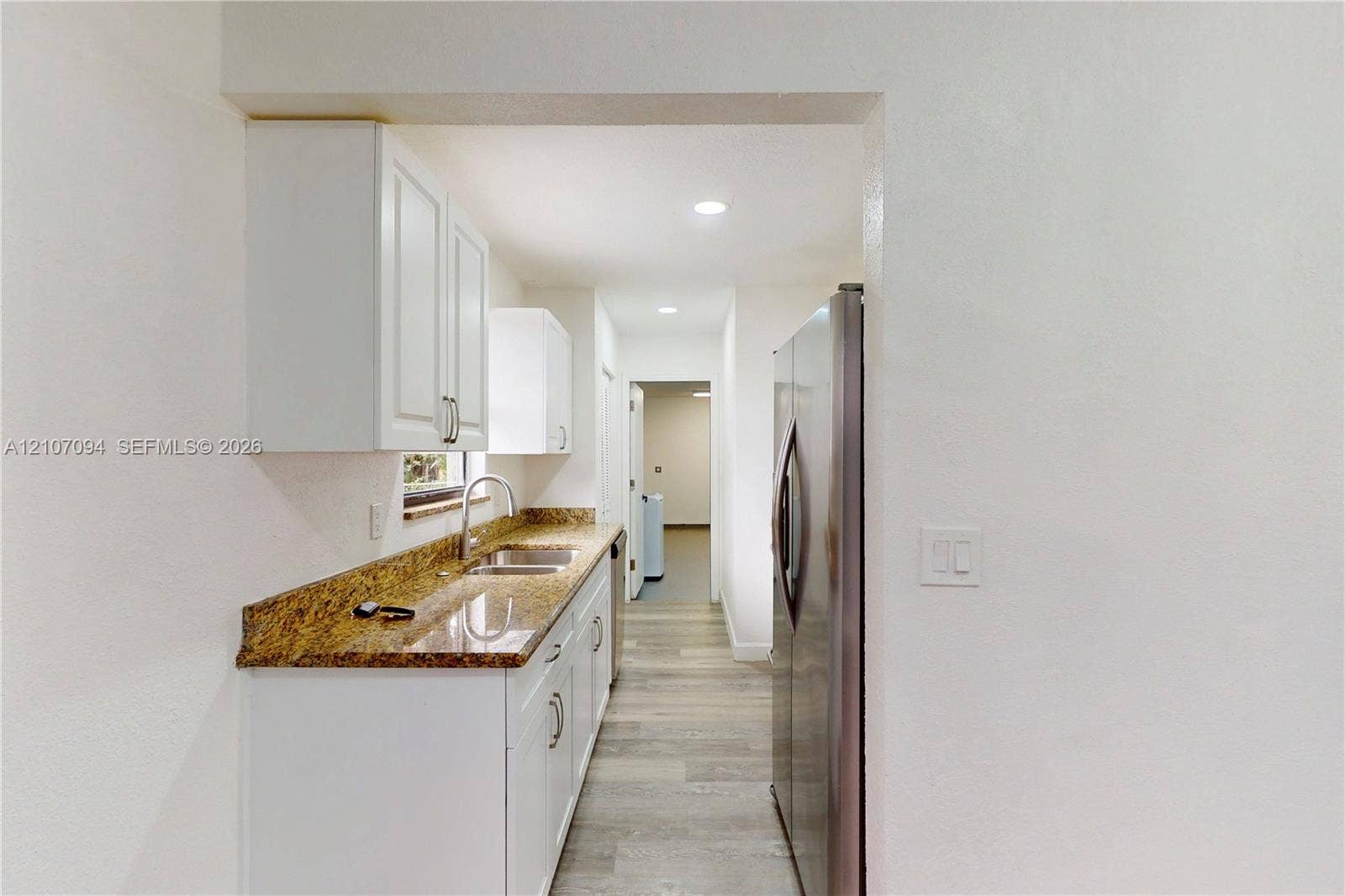1131 SW London Lane, Port St Lucie, FL 34953 Kitchen featuring white shaker-style cabinetry, stone-finish countertops, stainless steel side-by-side refrigerator, dual-basin sink with arched faucet, and wood-finish flooring