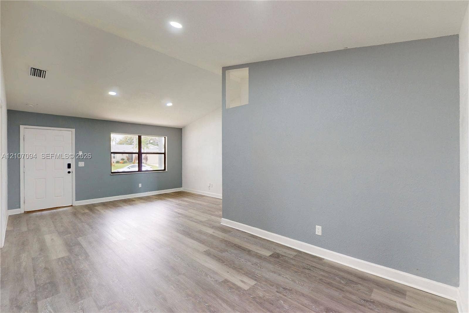 1131 SW London Lane, Port St Lucie, FL 34953 Interior space featuring vaulted ceilings, wood-finish flooring, recessed lighting, and large windows with dark-finish frames