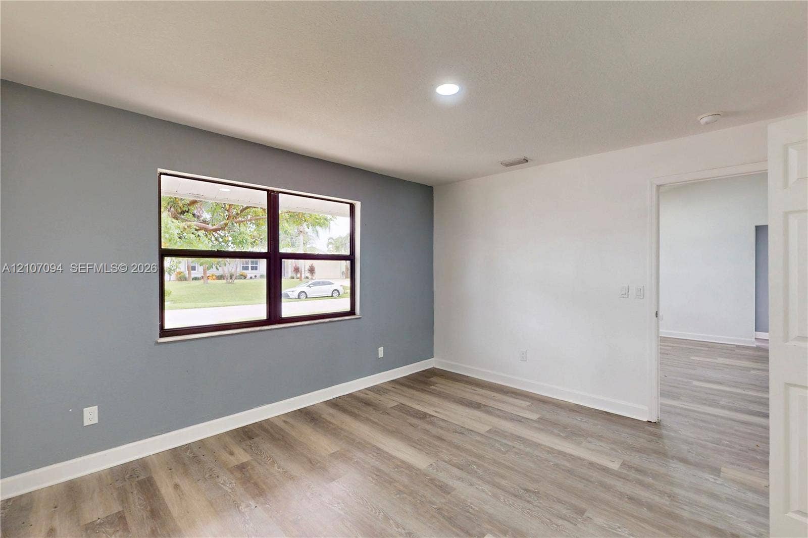 1131 SW London Lane, Port St Lucie, FL 34953 Neutral grey accent wall, expansive window, recessed lighting, and wood-finish flooring
