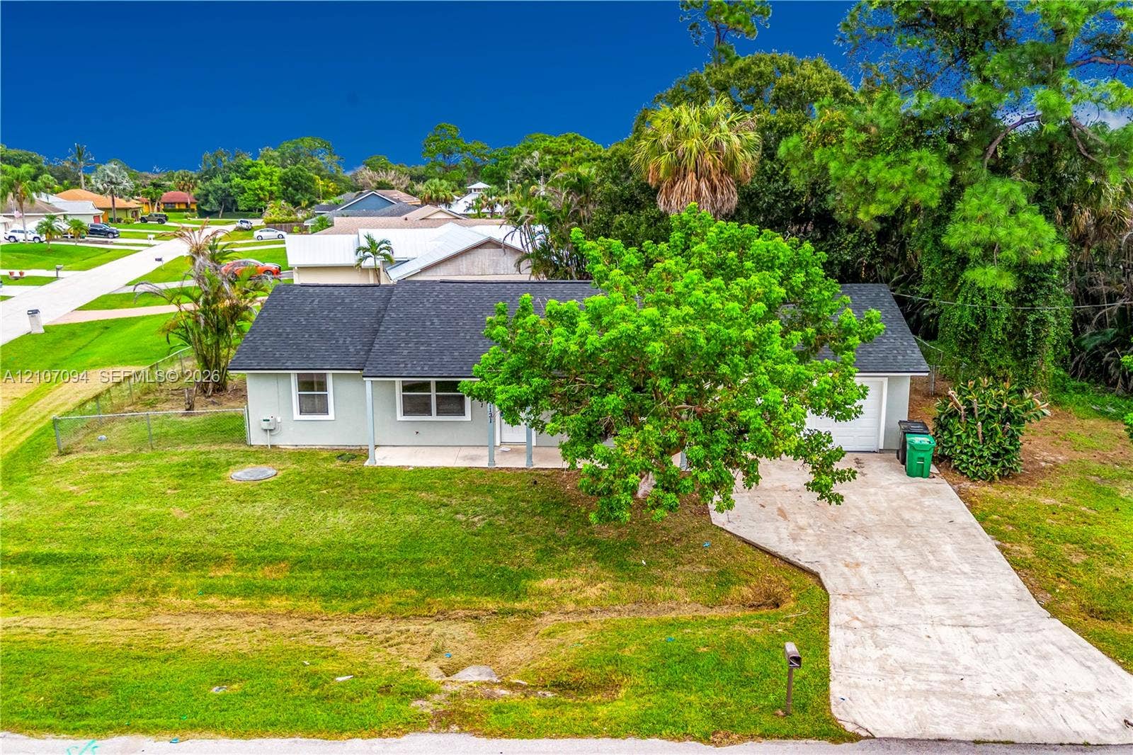 1131 SW London Lane, Port St Lucie, FL 34953 Single-story residence featuring a light-toned exterior, shingled roof, concrete driveway, and covered front entry