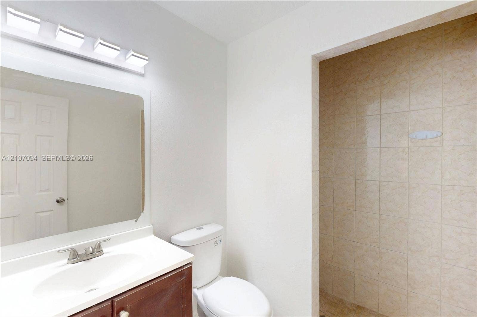 1131 SW London Lane, Port St Lucie, FL 34953 Bathroom featuring a vanity with an integrated sink, wall-mounted four-light fixture, framed mirror, and tiled shower enclosure