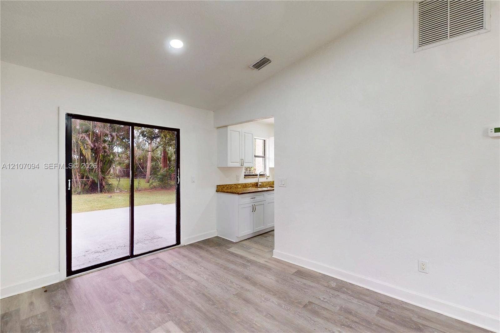 1131 SW London Lane, Port St Lucie, FL 34953 Vaulted ceiling, sliding glass doors, wood-finish flooring, and white cabinetry with stone-finish countertops