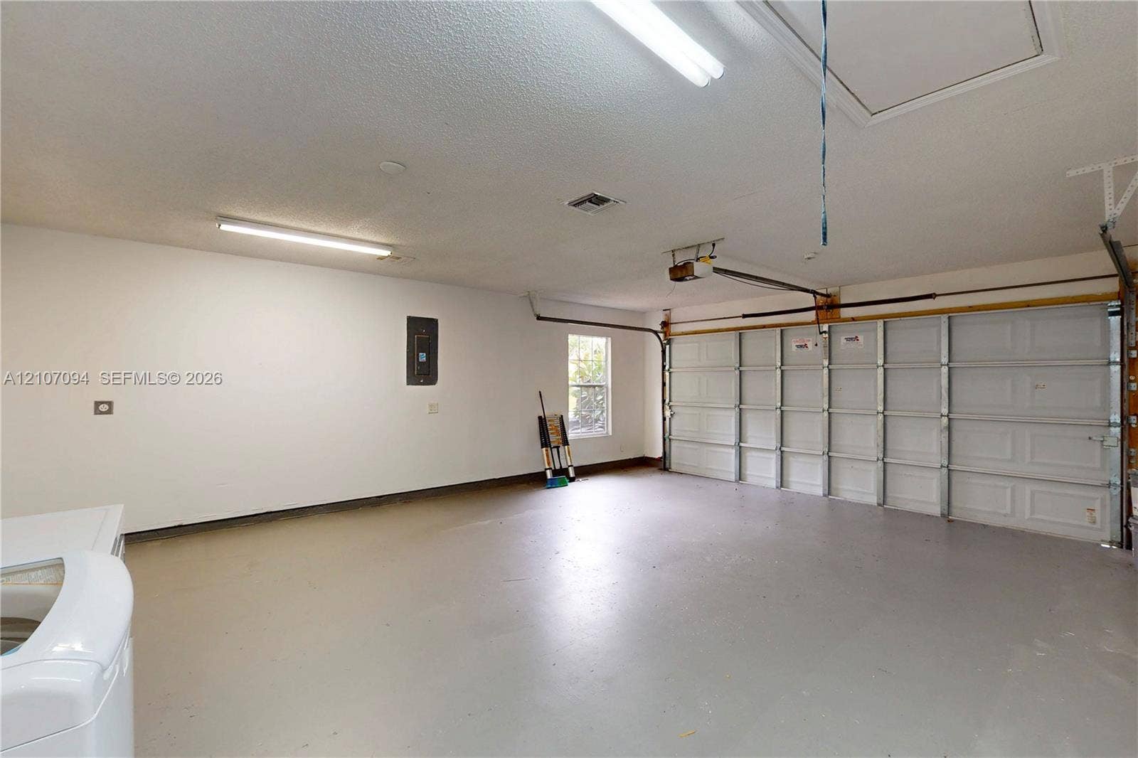 1131 SW London Lane, Port St Lucie, FL 34953 Multi-vehicle garage featuring a paneled sectional door, overhead fluorescent lighting, finished flooring, and an integrated electrical panel