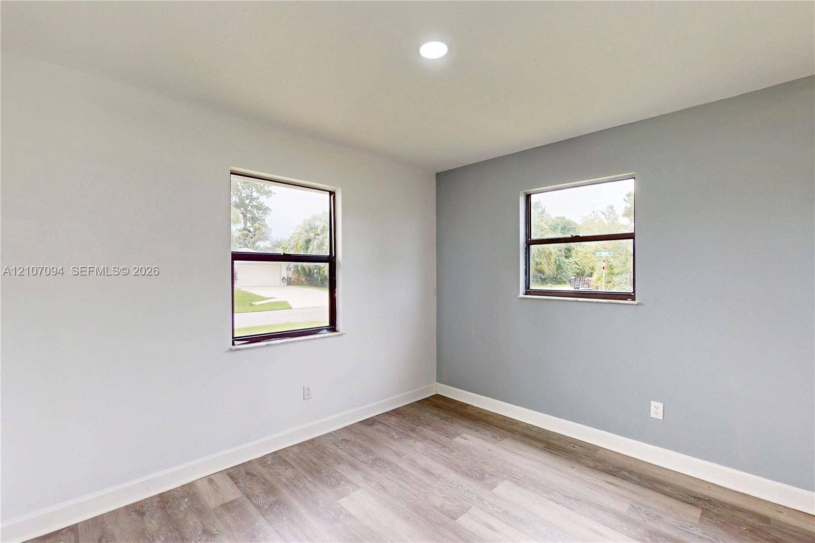 1131 SW London Lane, Port St Lucie, FL 34953 Room featuring wood-finish flooring, recessed lighting, and dual windows with dark frames, accented by a neutral-toned feature wall
