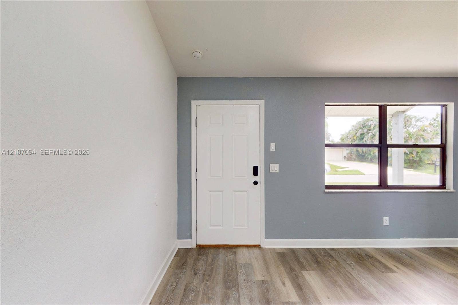 1131 SW London Lane, Port St Lucie, FL 34953 Entrance featuring a solid-panel door with integrated smart lock, wood-finish flooring, and large horizontal window with dark frame accents