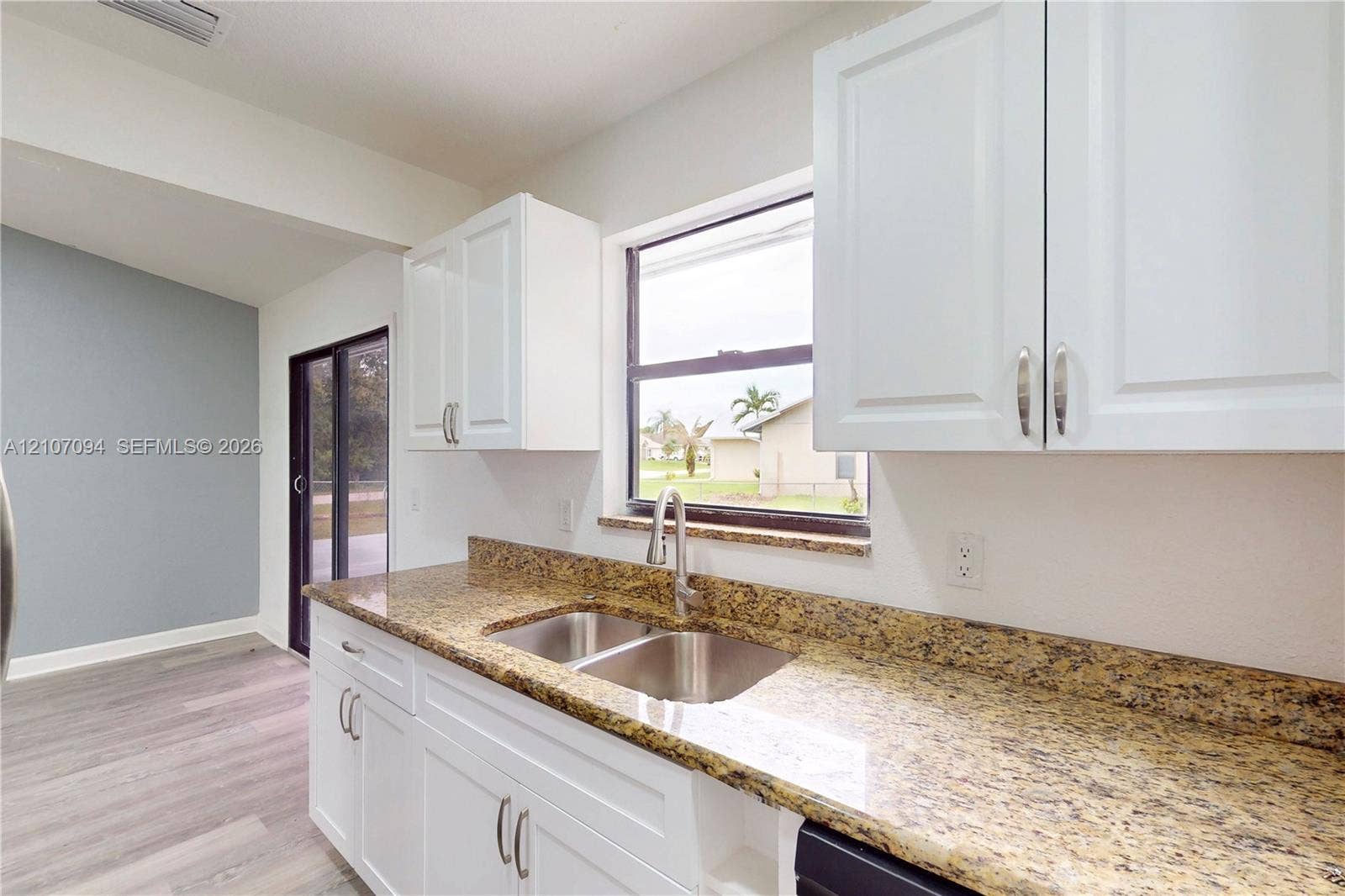 1131 SW London Lane, Port St Lucie, FL 34953 Kitchen featuring white Shaker-style cabinetry, stone-finish countertops, stainless steel dual-basin undermount sink with a gooseneck faucet, and wood-finish flooring