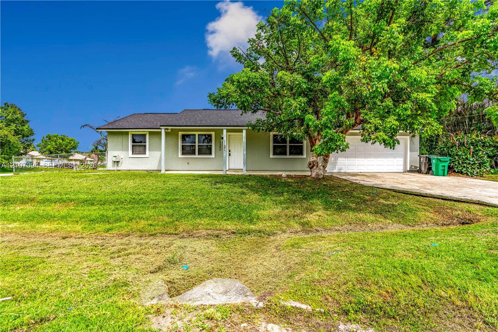 1131 SW London Lane, Port St Lucie, FL 34953 Single-story residence featuring a light-toned facade, an attached two-car garage, white-trimmed windows, a covered front entry, and mature landscaping