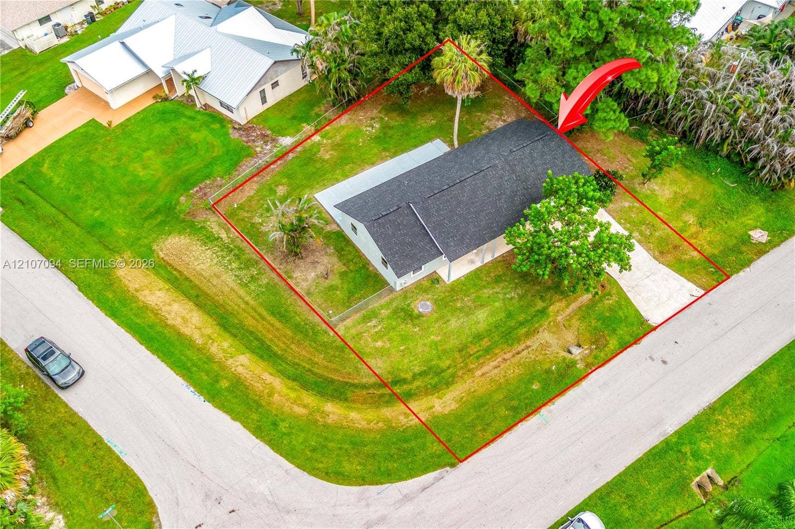 1131 SW London Lane, Port St Lucie, FL 34953 Aerial perspective of a corner lot property featuring a single-story residence with a shingled roof, concrete driveway, and expansive grass lawn