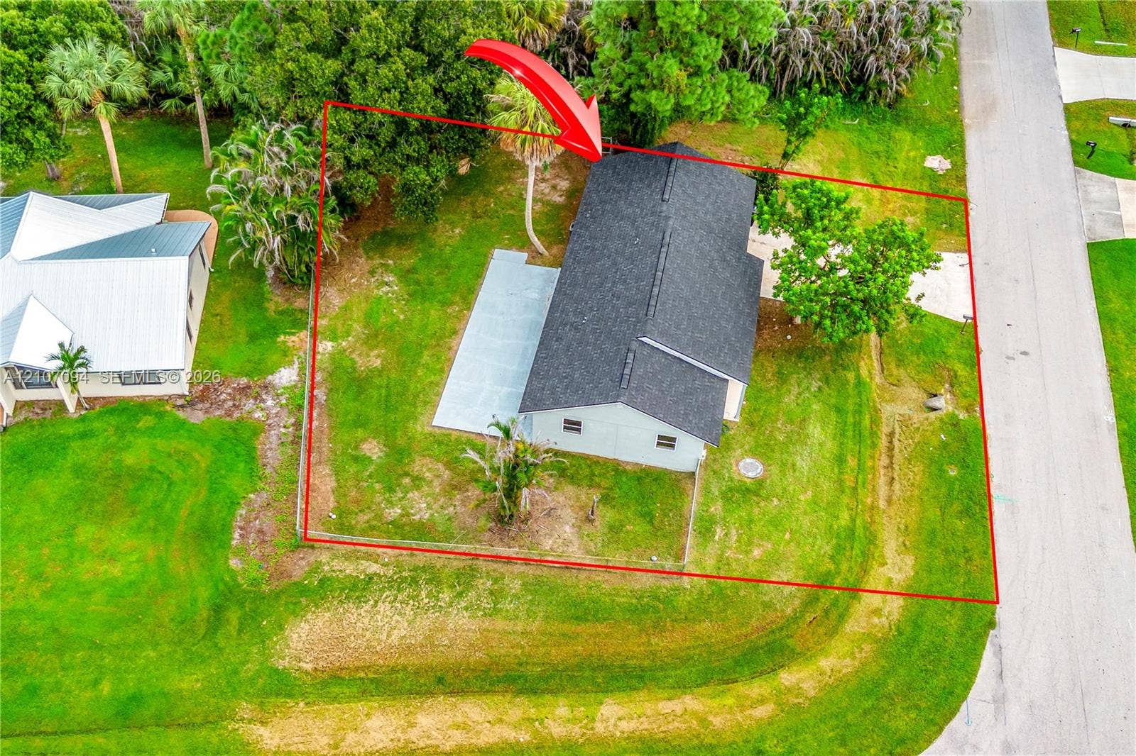 1131 SW London Lane, Port St Lucie, FL 34953 Aerial view of property featuring a detached residence with a composite shingle roof, concrete patio, concrete driveway, and mature landscaping on a grass-covered lot