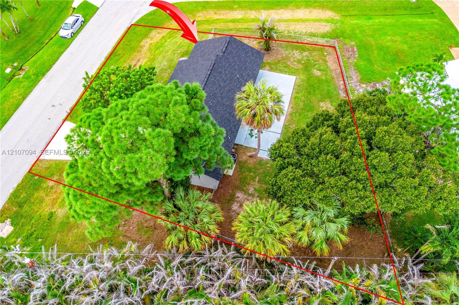 1131 SW London Lane, Port St Lucie, FL 34953 Aerial perspective of the property featuring a dark-toned shingled roof, a concrete patio, and a landscaped lot with mature palm and broadleaf trees