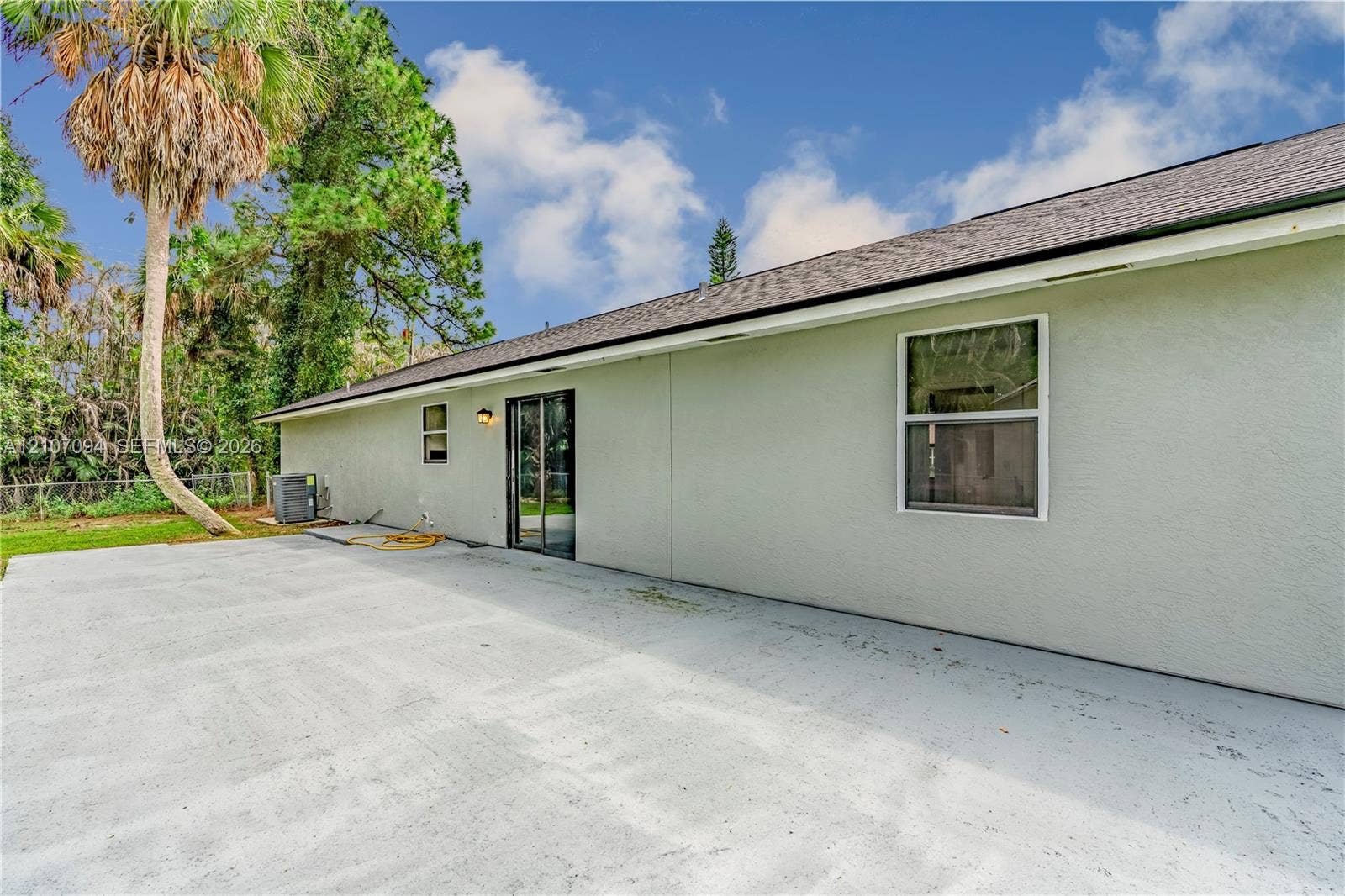1131 SW London Lane, Port St Lucie, FL 34953 Rear exterior featuring a spacious concrete patio, stucco siding, sliding glass doors, and shingle roofing
