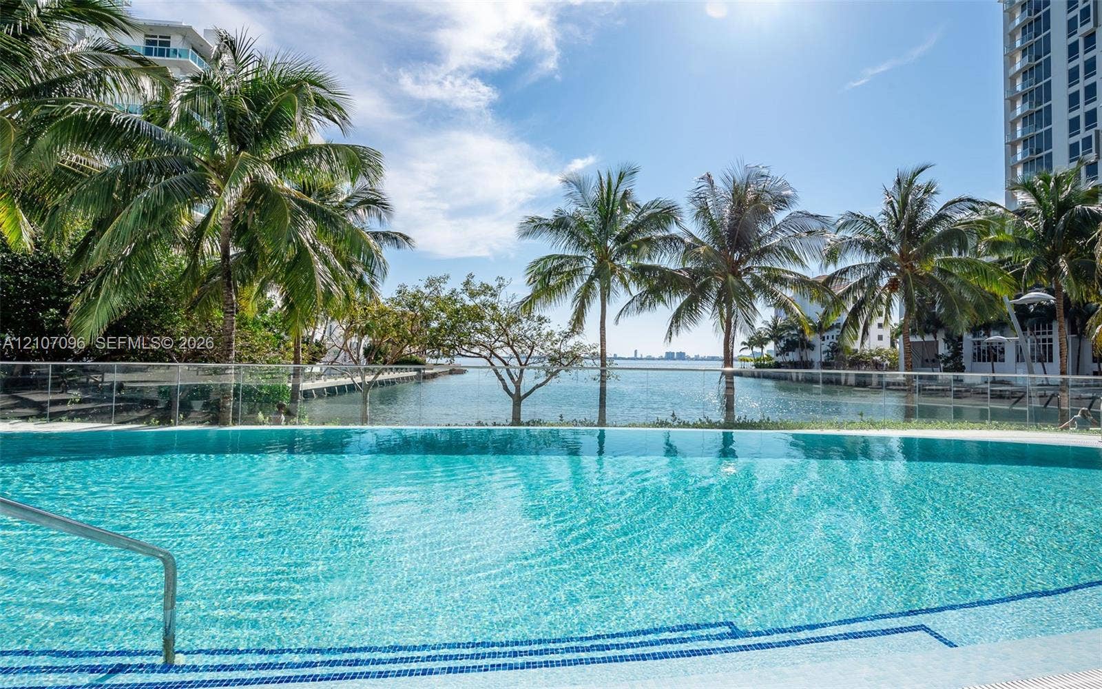 Curved swimming pool featuring a tiled interior, built-in steps, metal handrail, and a transparent glass panel railing overlooking the water