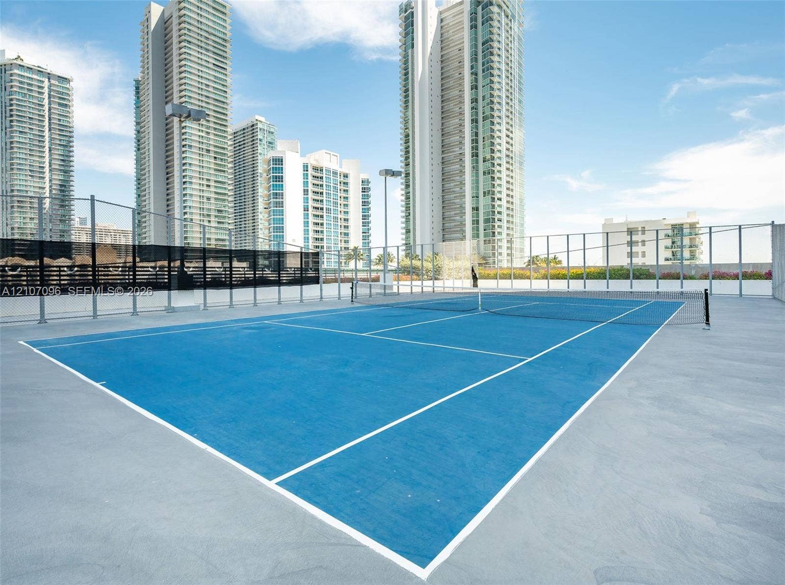 Rooftop tennis court featuring a hard surface, integrated net, perimeter fencing, and stadium-style lighting