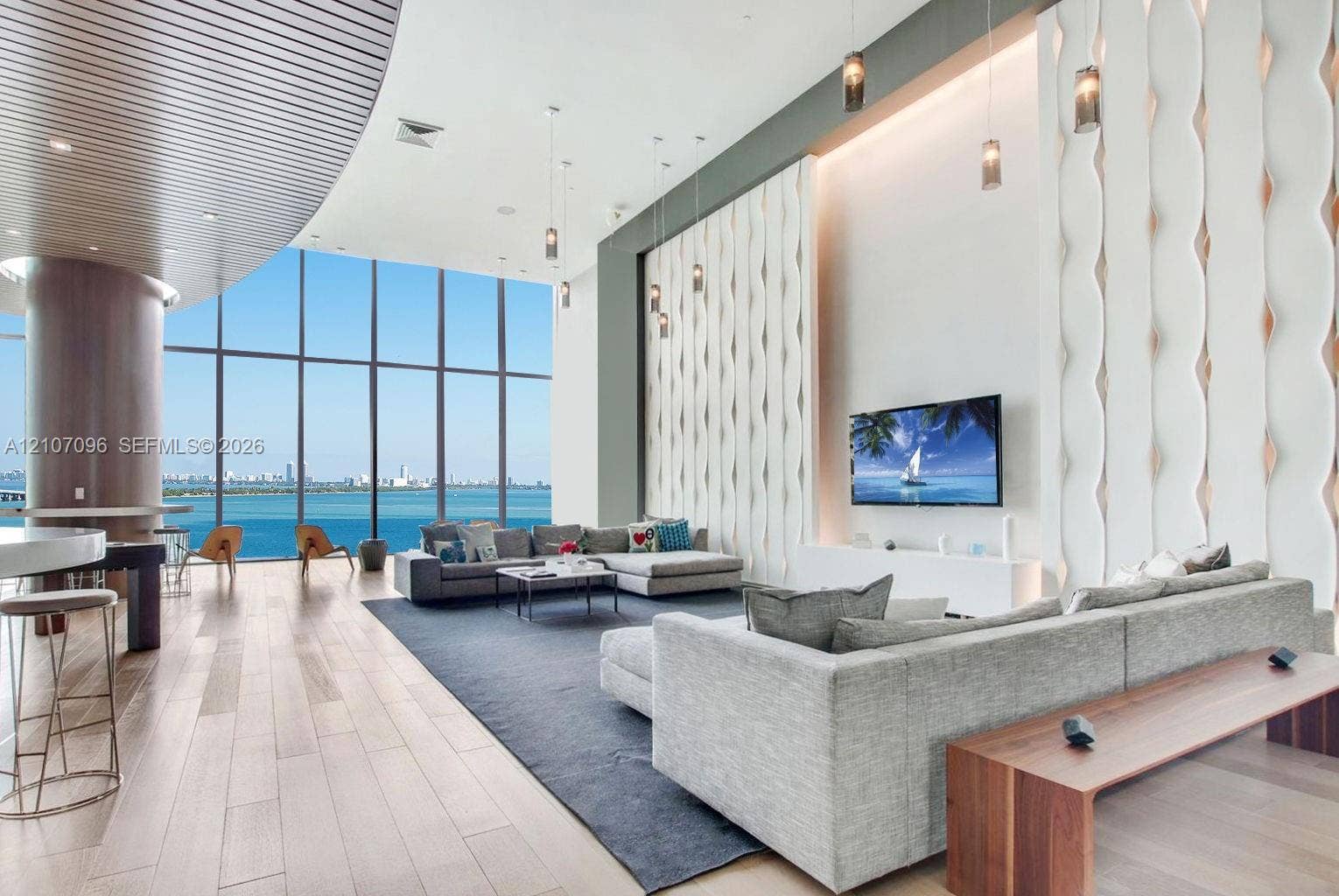 Expansive floor-to-ceiling windows featuring panoramic water scenery, wood-finish flooring, curved ceiling detail, and floor-to-ceiling textured accent wall with integrated pendant lighting