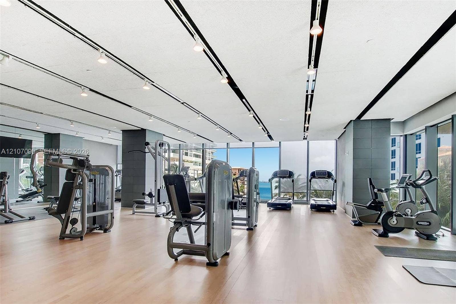 Fitness center featuring floor-to-ceiling windows, wood-finish flooring, recessed track lighting, and tiled structural columns