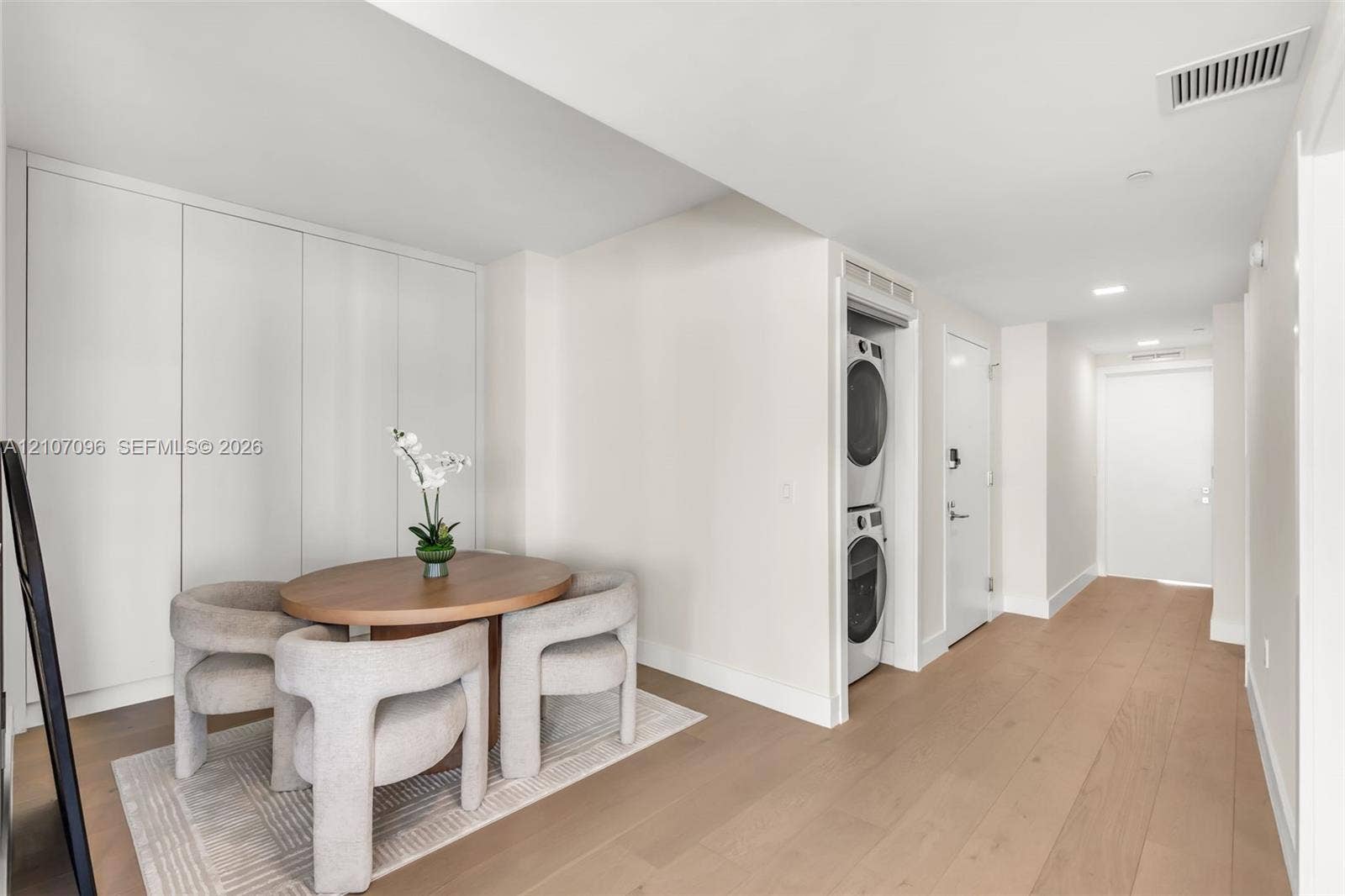 Full-height white built-in cabinetry, wood-finish flooring, and stacked laundry unit housed within a recessed closet