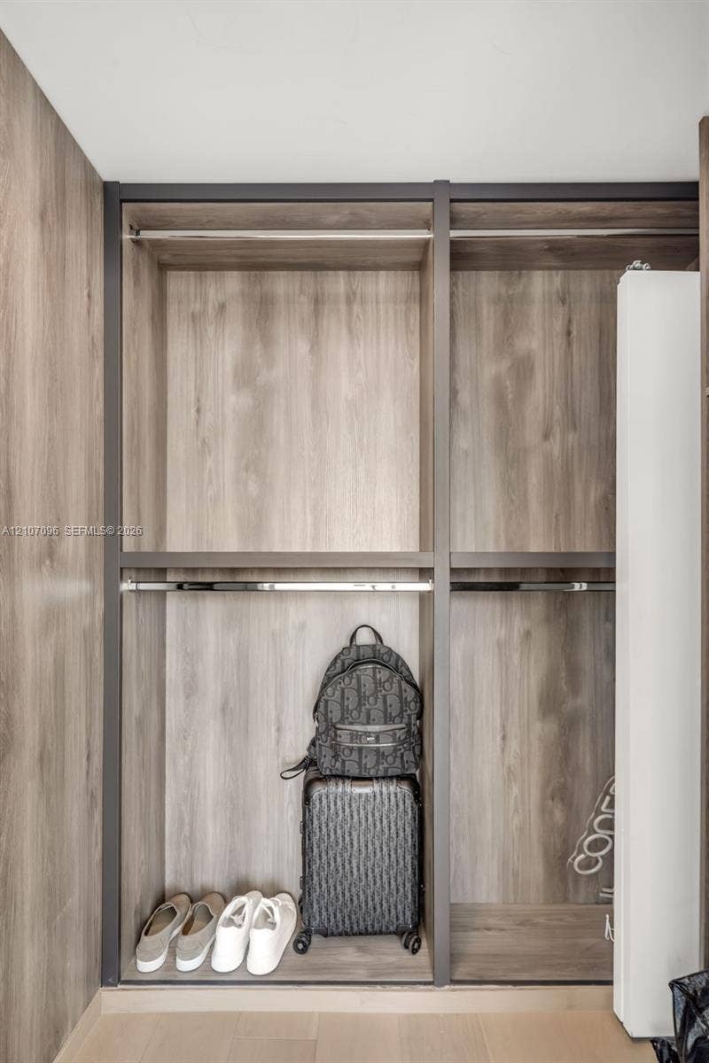 Built-in closet featuring wood-finish laminate cabinetry, metal frame detailing, and dual-level metal hanging rods