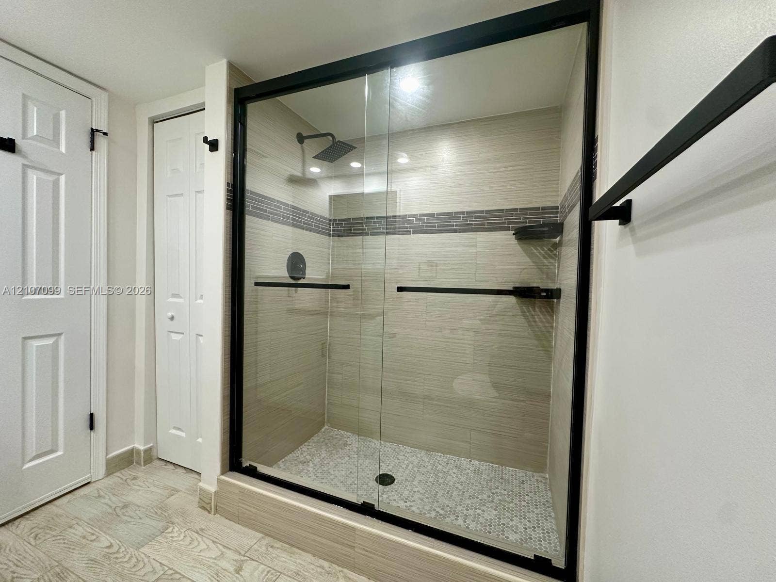 Walk-in shower featuring a sliding glass enclosure with matte black hardware, textured wall tile with a mosaic inlay, pebble-style floor tile, and a square rainfall shower head