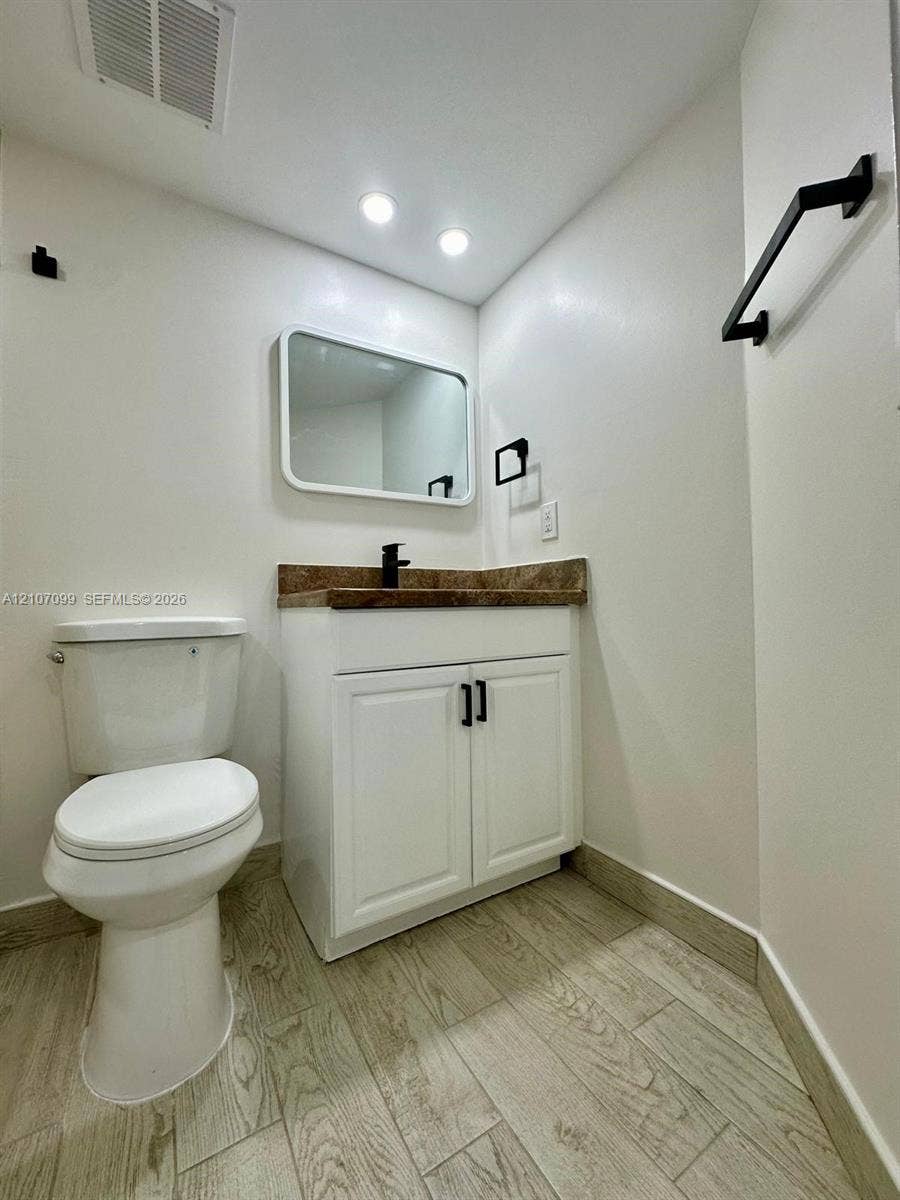 White vanity cabinet with stone-finish countertop, undermount sink, matte black hardware, and wood-finish flooring