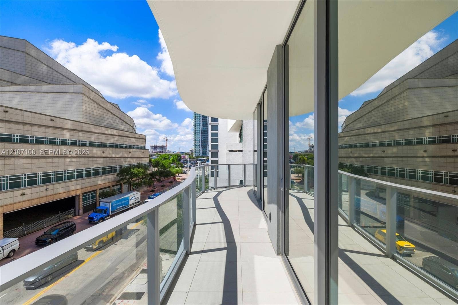 Curved balcony featuring tile flooring, full-height glass sliding doors, and a glass-paneled railing