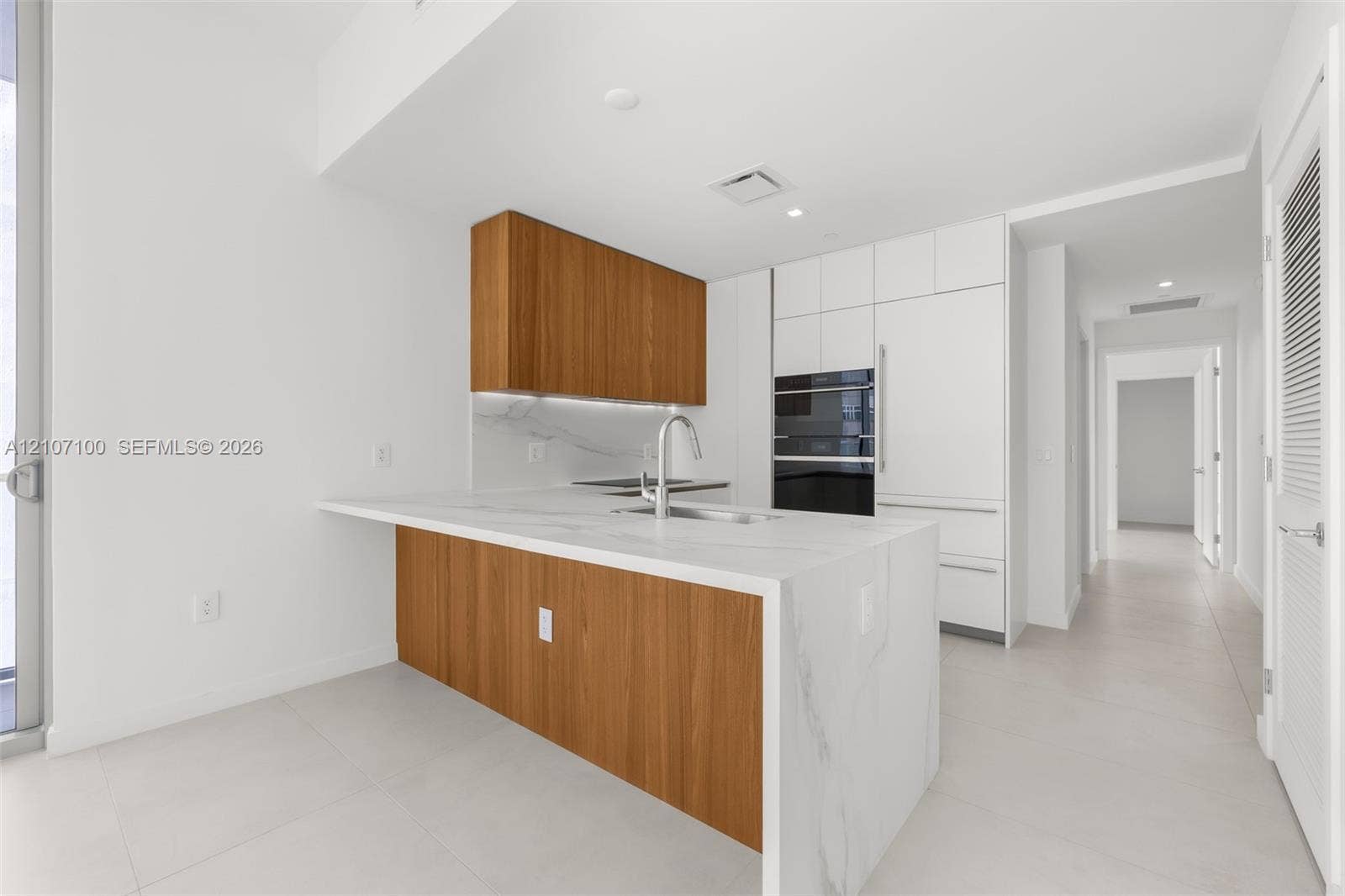Kitchen featuring a waterfall island with stone-surface countertop, wood-finish cabinetry, built-in double wall ovens, panel-ready refrigerator, and under-cabinet lighting