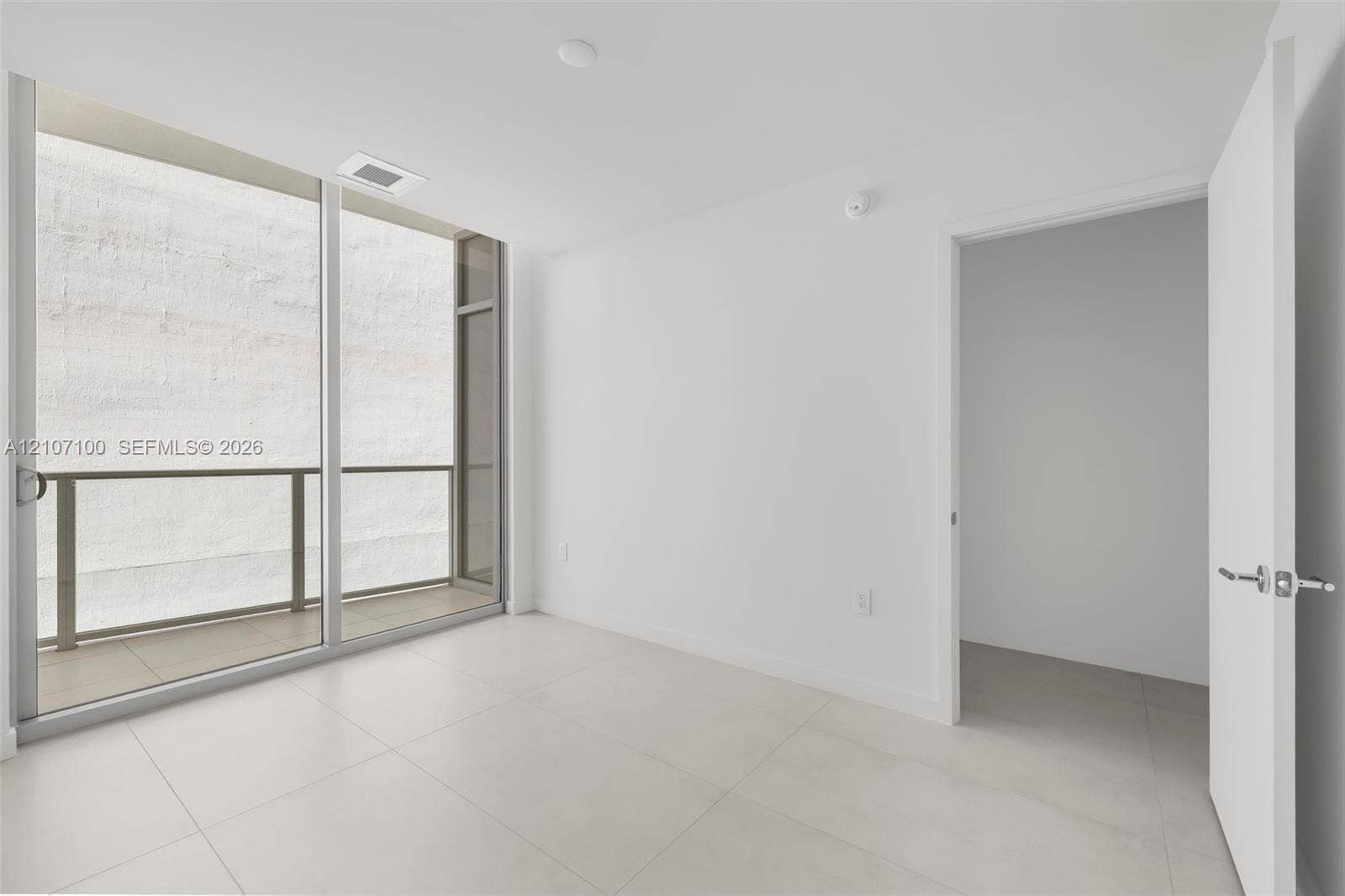 Large-format tile flooring, floor-to-ceiling glass sliding door, and private balcony with metal railing