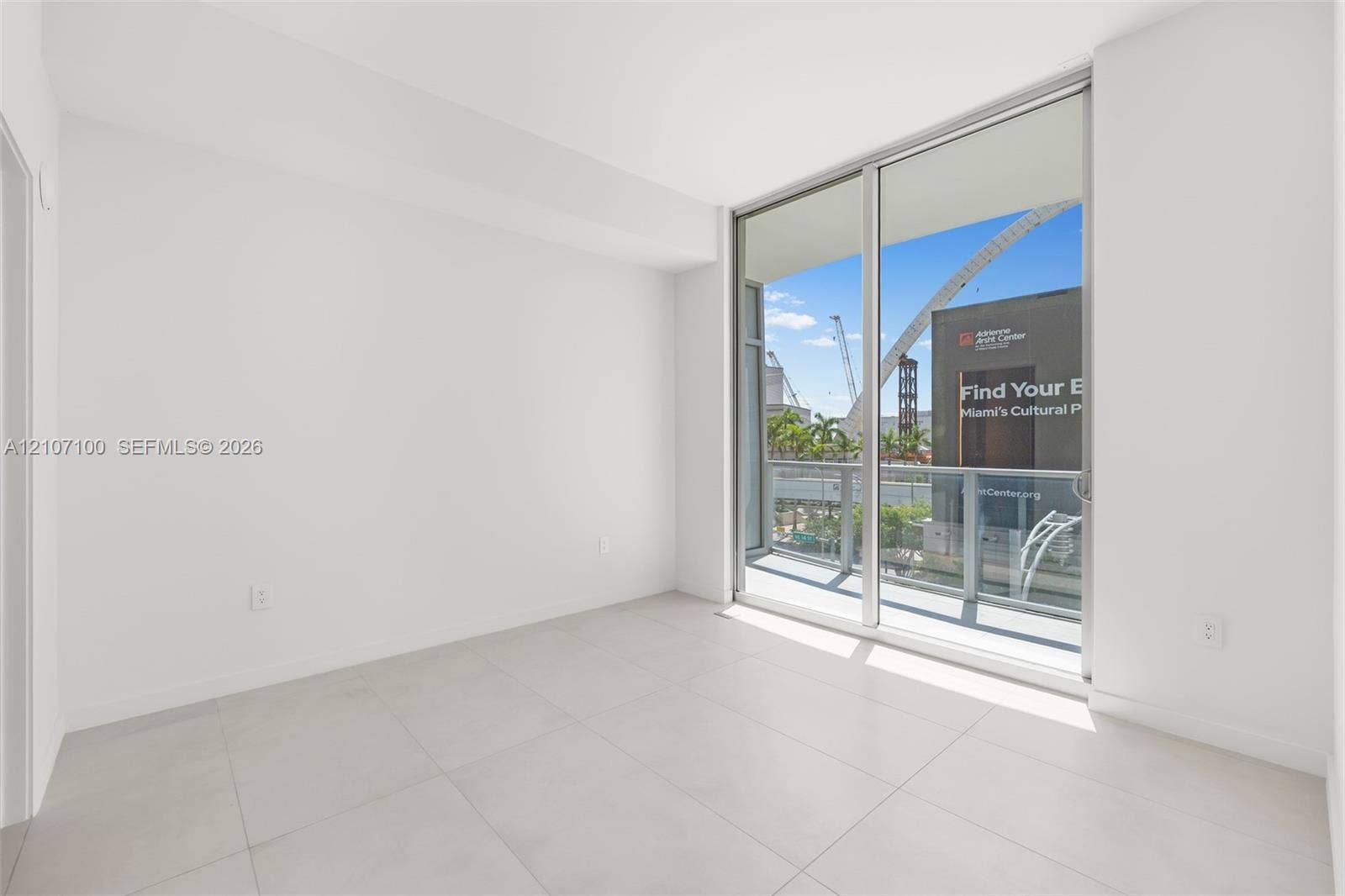 Floor-to-ceiling sliding glass doors, large format neutral floor tiling, and a private balcony featuring metal railing