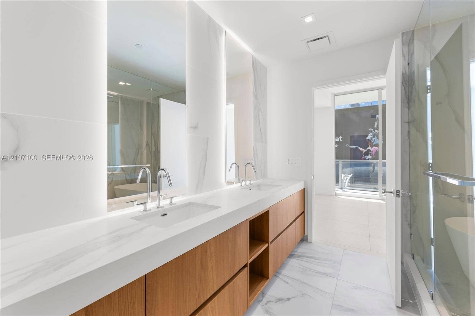 Double vanity featuring wood-finish cabinetry, solid-surface countertops with integrated rectangular sinks, integrated vertical mirror lighting, and floor-to-ceiling large-format stone-patterned tiling