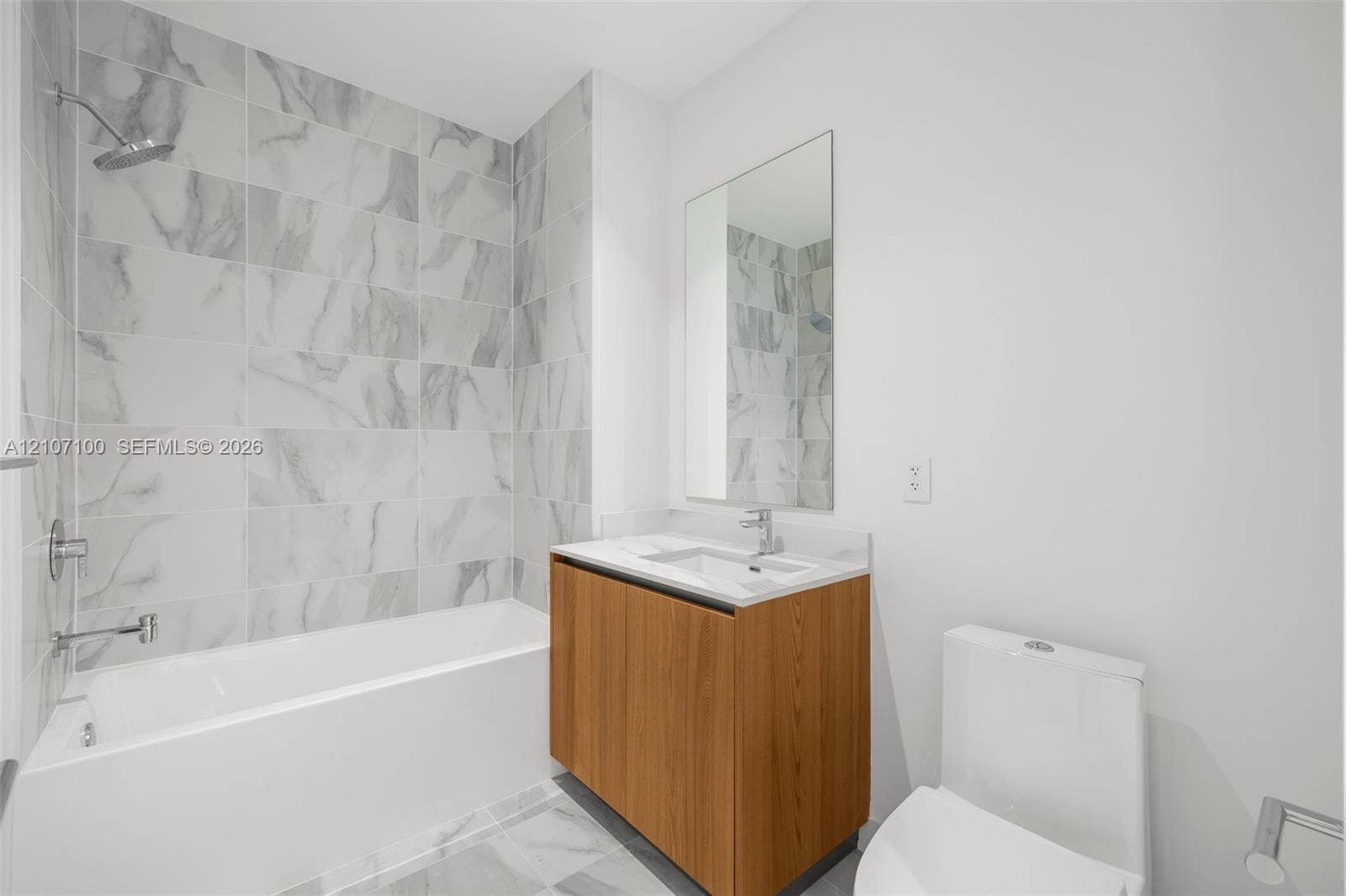 Bathroom featuring a tub-shower combination with large-format tile surround, wood-finish vanity with an integrated basin, countertop, and a wall-mounted mirror
