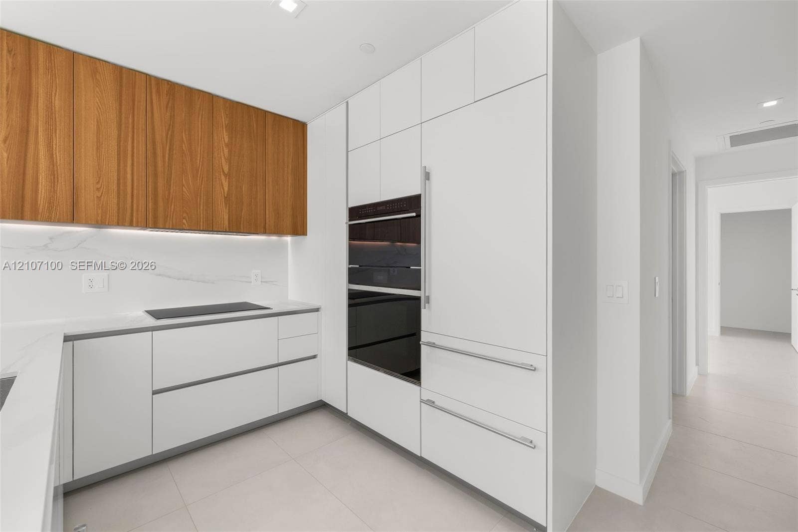 Modern kitchen featuring white flat-panel cabinetry, wood-finish upper cabinets, integrated appliances, stone-surface backsplash, and built-in wall oven