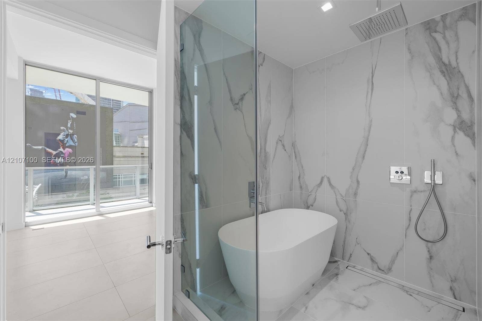 Enclosed shower featuring large-format stone-finish tile, freestanding soaking tub, rain showerhead, handheld sprayer, and glass partition