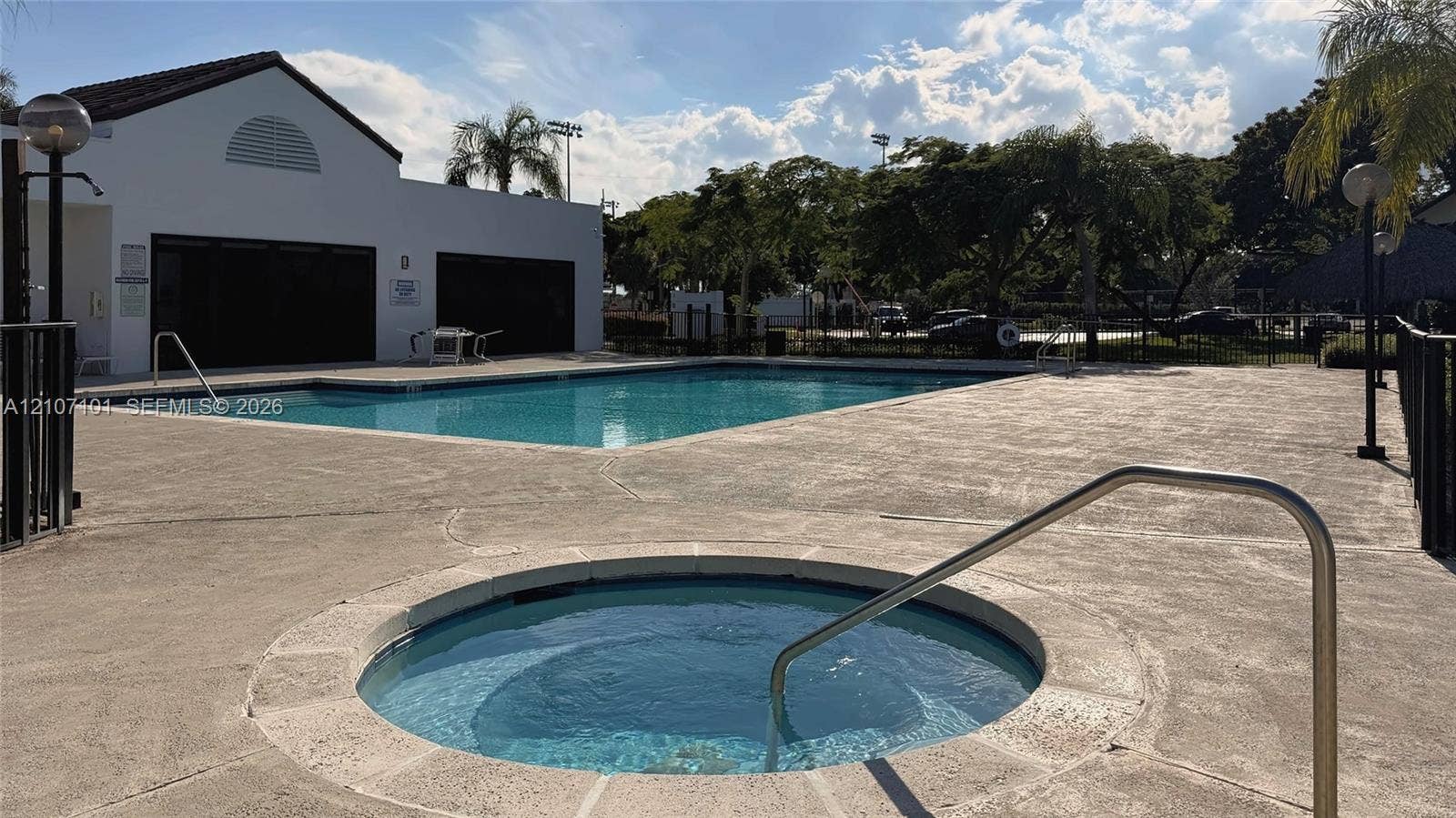 In-ground swimming pool and circular spa featuring concrete decking, metal safety rails, and perimeter lighting