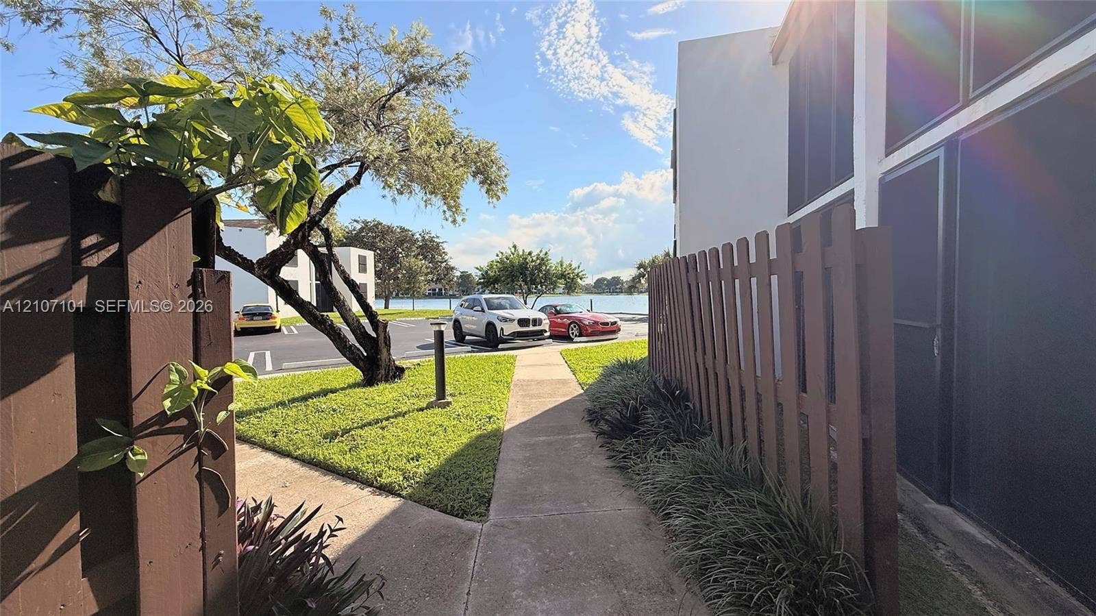 Concrete pathway flanked by a wood privacy fence and manicured lawn, featuring a waterfront location