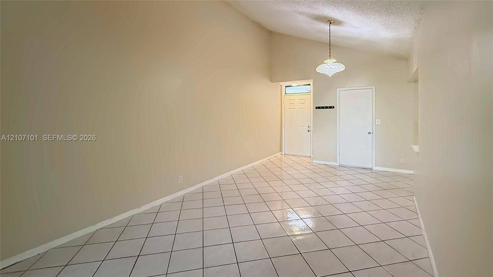 Vaulted ceilings featuring a pendant light fixture, ceramic tile flooring set on a diagonal pattern, and an exterior door with an overhead transom window