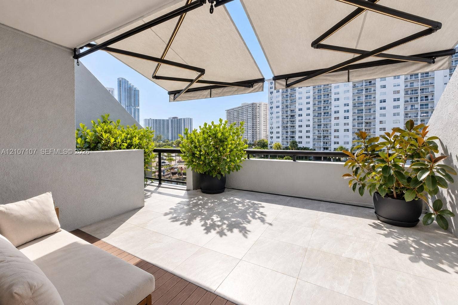 Covered balcony featuring large-format stone-style tile flooring, wood-finish decking accents, a retractable fabric awning, and a metal railing