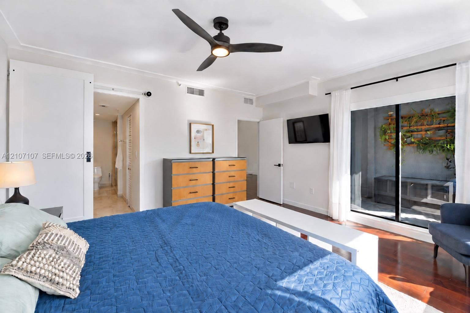 Spacious room featuring wood-finish flooring, a matte black three-blade ceiling fan with integrated lighting, and a sliding barn-style door