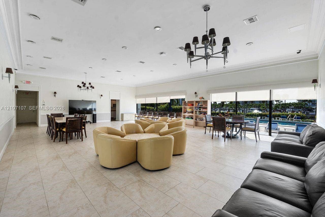 Expansive common area featuring large-format tile flooring, multi-arm tiered chandeliers, crown molding, and floor-to-ceiling glass sliding doors