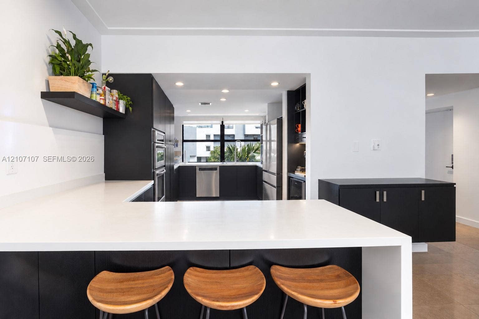 Kitchen featuring matte black cabinetry, solid-surface countertops with a waterfall edge, stainless steel built-in appliances, recessed lighting, and a floating wall-mounted display shelf