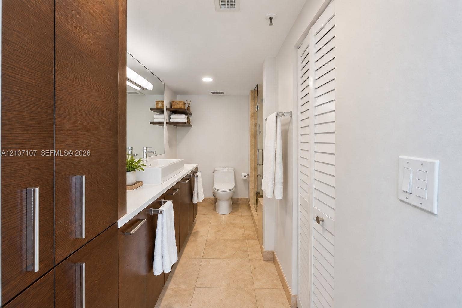 Bathroom featuring dark wood-finish cabinetry, a rectangular vessel sink with a countertop, stone-tile flooring, and white louvered doors