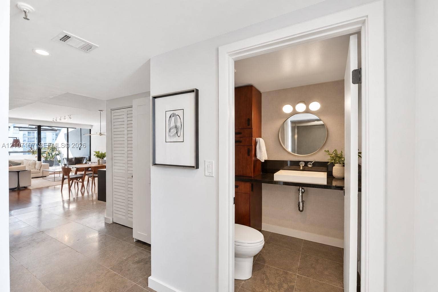 Bathroom featuring a round mirror, integrated dark stone countertop, square vessel sink, and full-height wood-finish cabinetry