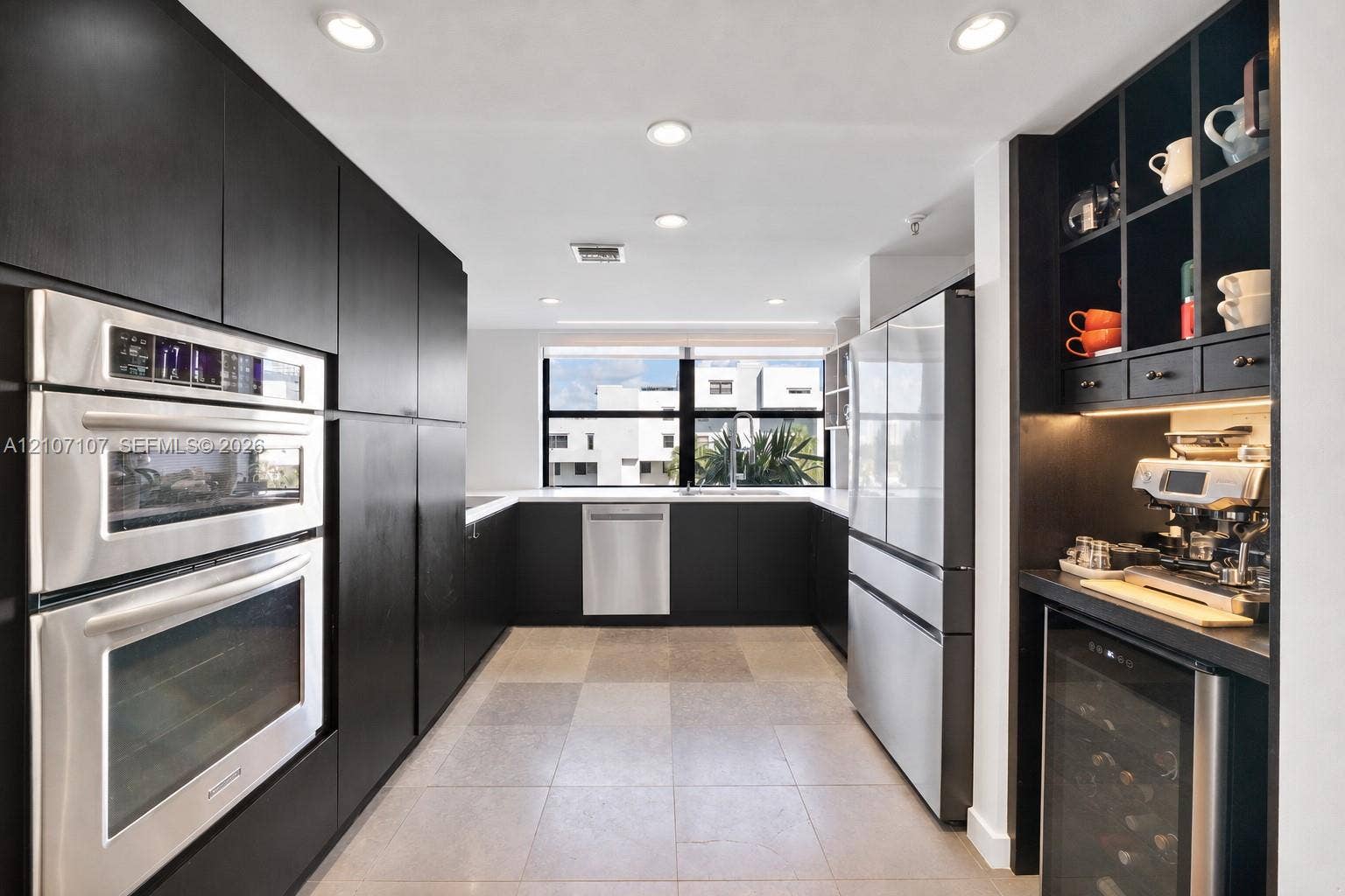 Kitchen featuring flat-panel dark cabinetry, built-in double wall ovens, integrated stainless steel appliances, under-cabinet lighting, and built-in beverage refrigerator