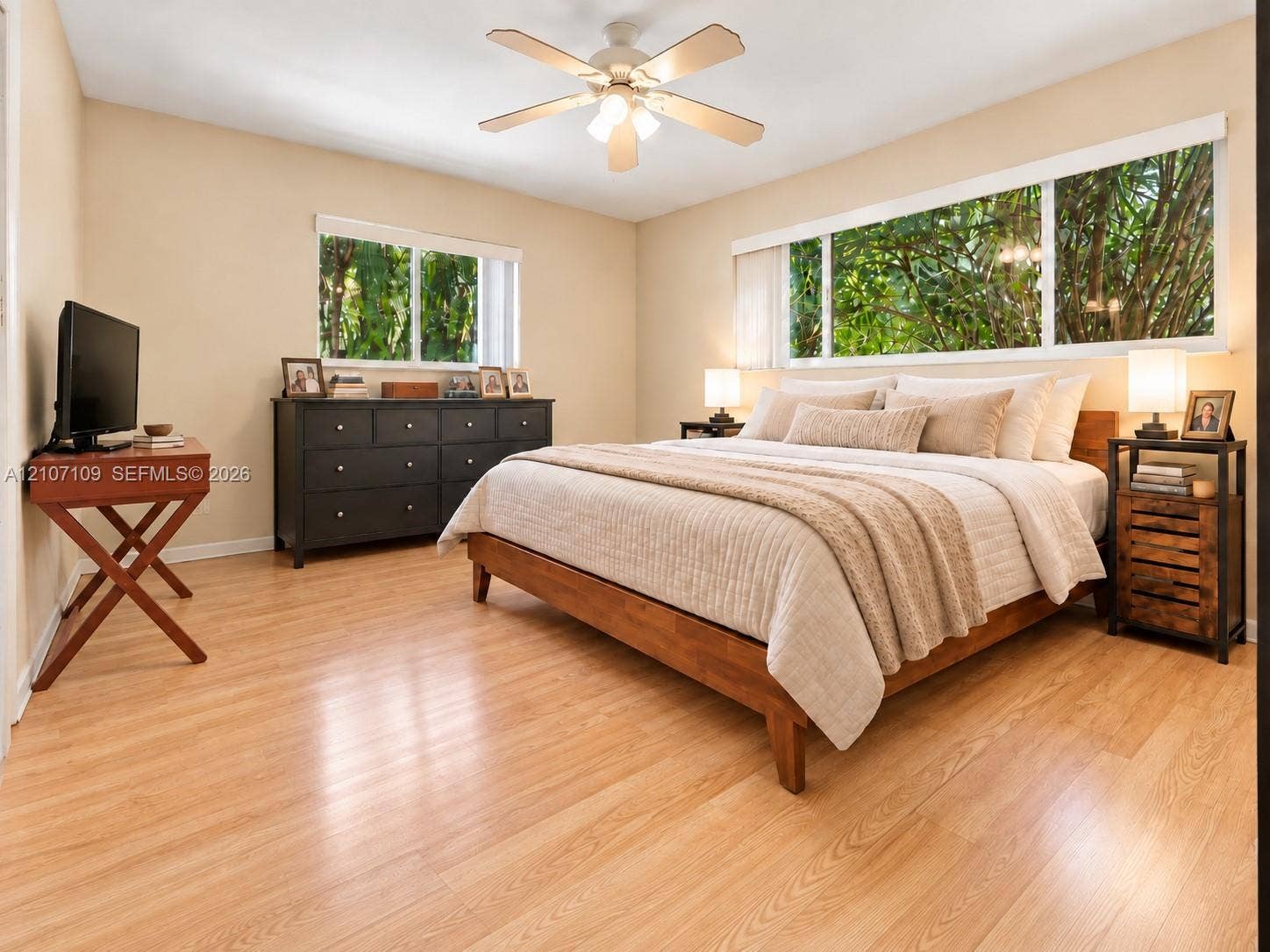 Wood-finish flooring, multi-pane windows with exterior greenery, and a ceiling-mounted light fixture with integrated fan