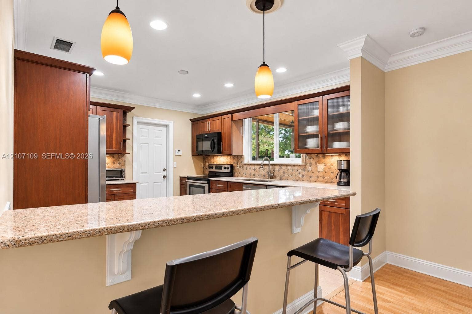 Kitchen featuring warm-tone wood cabinetry, stone-surfaced peninsula countertop, crown molding, recessed lighting, and pendant fixtures