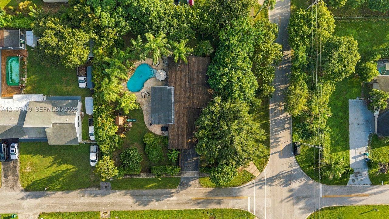 Aerial perspective featuring an expansive lot with a swimming pool, paved patio, mature trees, and a multi-section asphalt shingle roof