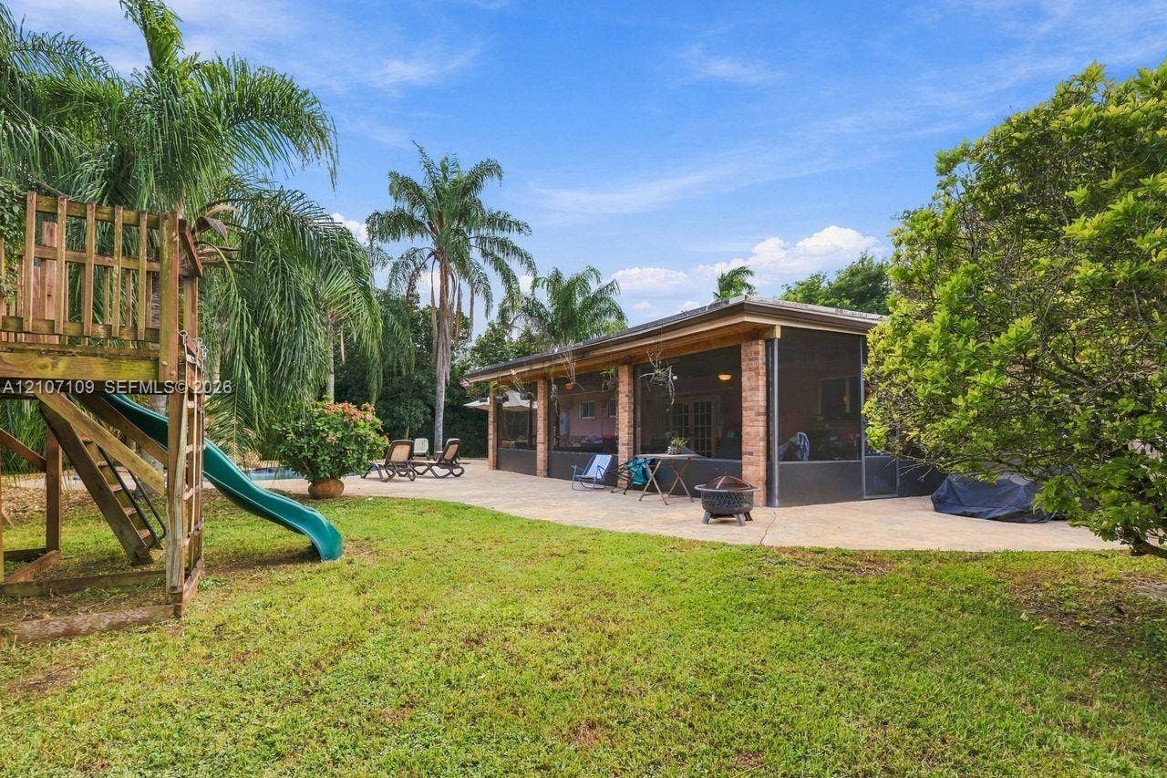Backyard featuring a screened-in patio, expansive concrete hardscaping, brick exterior accents, and mature landscaping