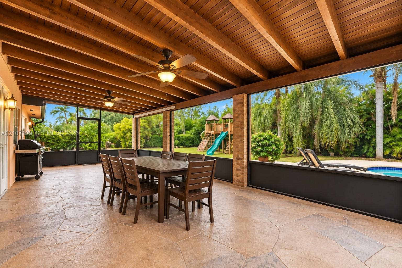 Covered patio featuring an exposed wood-beam ceiling, stamped concrete flooring, brick support columns, and full-height screen enclosure