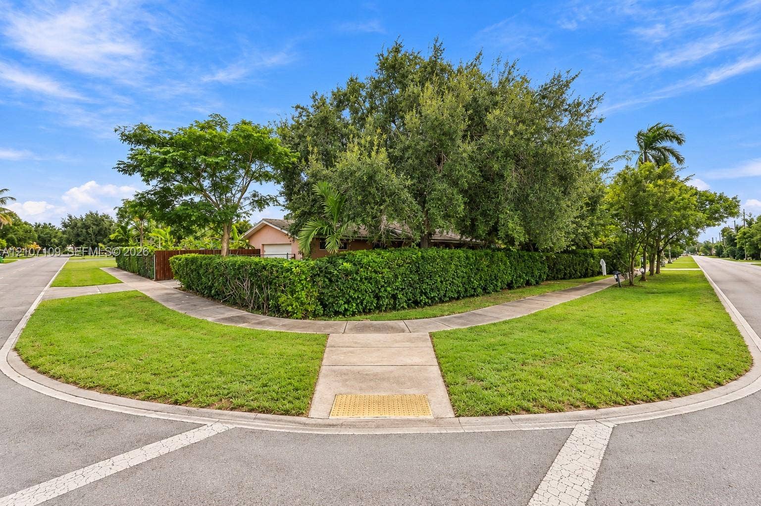Corner lot featuring mature trees, manicured hedges, and concrete walkways