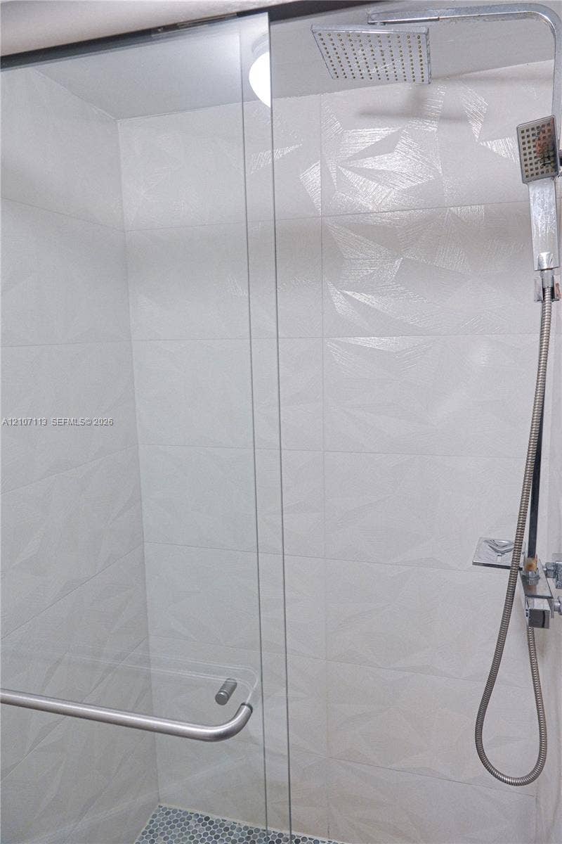 10451 W Broward Boulevard, #102, Plantation, Plantation, FL 33324 Walk-in shower featuring textured geometric wall tile, frameless glass door, rain-style showerhead, handheld sprayer, and mosaic tile flooring