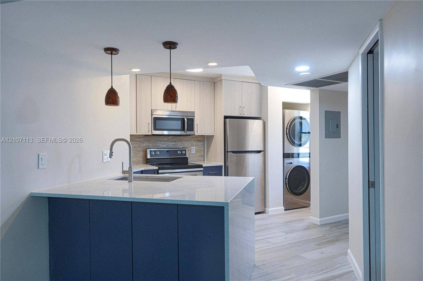 10451 W Broward Boulevard, #102, Plantation, Plantation, FL 33324 Kitchen featuring an island with a stone-finish countertop, stainless steel appliances, neutral cabinetry, stacked laundry unit, and wood-finish flooring